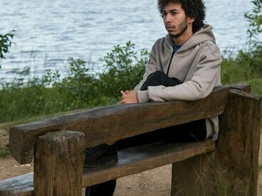 A young man sitting alone on a park bench beside a lake, representing the loneliness and uncertainty that can accompany the fear of abandonment