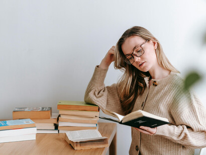A young woman reads a book surrounded by a pile of literature