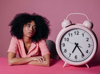 A woman stands before a giant pink alarm clock, representing time and its meaning