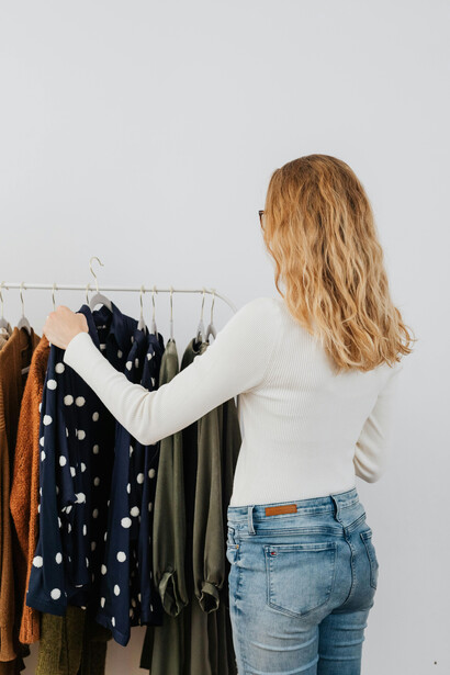 A woman wearing a white long-sleeved shirt stands next to a clothes rack