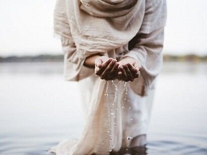 A person walks through the water, draped in a biblical robe