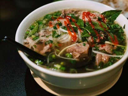 A bowl of pho presented with a plate of herbs and noodles, showcasing the variety of ingredients that make this dish so popular