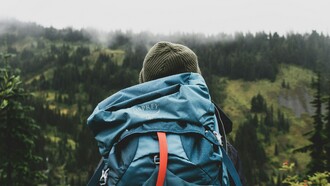 A lone backpacker stands still overlooking a vast landscape, taking in the distance not as a destination to conquer but as a moment to fully experience and carry forward