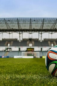 A lone soccer ball waits on the pitch, with an empty stadium looming in the background