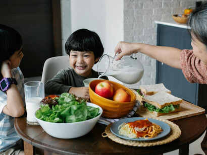 An elderly grandmother sitting at the table eating a healthy salad with her Asian grandchildren, while a delighted little girl watches her