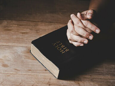 Hands folded in prayer on a Holy Bible inside a church, symbolizing faith and Christian spirituality