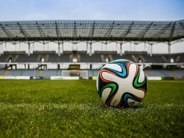 Em primeiro plano, uma bola de futebol se destaca sobre a grama, enquanto o estádio aparece desfocado ao fundo. É dentro desse cenário que as decisões de treinador, jogadores e diretoria precisam transformar expectativa em resultados