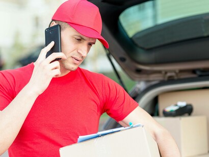 Addetto alle consegne parla al telefono mentre tiene in braccio un pacco e alcuni documenti