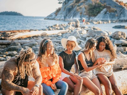 Friends gathered along a rocky shoreline beneath open skies, representing the healing comfort of human connection