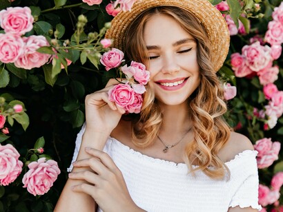 A woman in soft sunlight smiles amid blooming pink roses, embodying the lover’s archetype of vulnerability and beauty