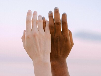 Hands of different skin tones intertwine, forming a bridge of solidarity against a serene backdrop, emphasizing how relations redefine the boundaries of humanity