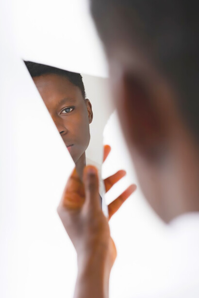Within the context of discussing African American identity, a young Black boy poignantly holds a mirror, his contemplative reflection symbolizing the nuanced journey of self-discovery explored in the article