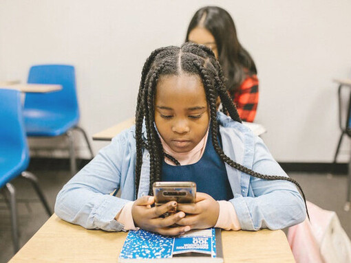 A small girl in the classroom, absorbed in her smartphone