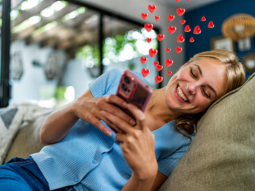 A teenage girl scrolls through social media on her smartphone at home, surrounded by digital icons representing likes, comments, and online engagement