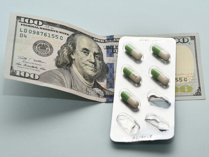 A stack of pills alongside a bundle of money on a table, representing the connection between healthcare and financial interests