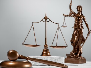 A judge's gavel resting before the scales of justice and Lady Justice, symbolizing the foundation of legitimacy through proportional legal order