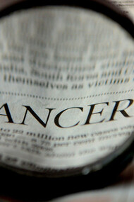Beneath the magnifying glass, the word 'cancer' becomes apparent on the newspaper