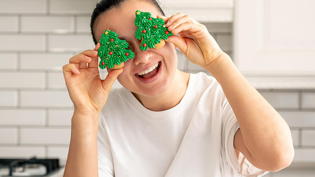 A woman decorates gingerbread cookies shaped like Christmas trees in the kitchen