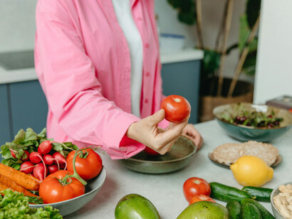A person wearing a pink overshirt holding a tomato while preparing a healthy meal