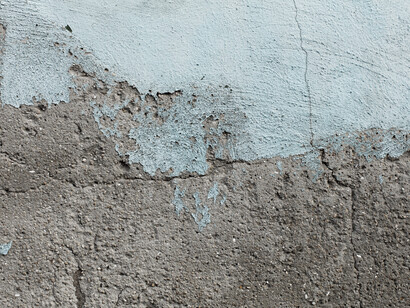 Una superficie muraria fatiscente con vernice azzurra che si sta scrostando, rivelando la trama del cemento sottostante
