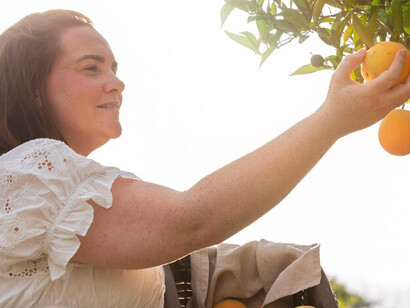 A woman carefully picks ripe fruits from a tree, enjoying the beauty of nature's harvest
