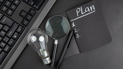 Top view of a business plan written on a black notepad with a laptop keyboard, light bulb, and pen on a black table