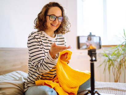 Young female blogger talking to her followers, live stream and showing yellow sweater on camera