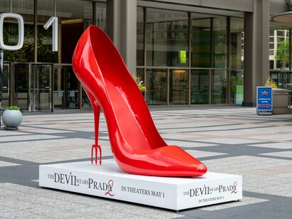 Escultura gigante de um sapato de salto alto vermelho instalada em praça pública para promover "O Diabo Veste Prada 2". O símbolo remete imediatamente ao universo da moda que consagrou a franquia