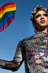 A man in drag wearing a sparkly outfit and waving the rainbow flag