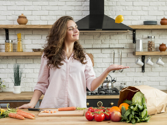 A brunette woman stands in the kitchen surrounded by healthy food