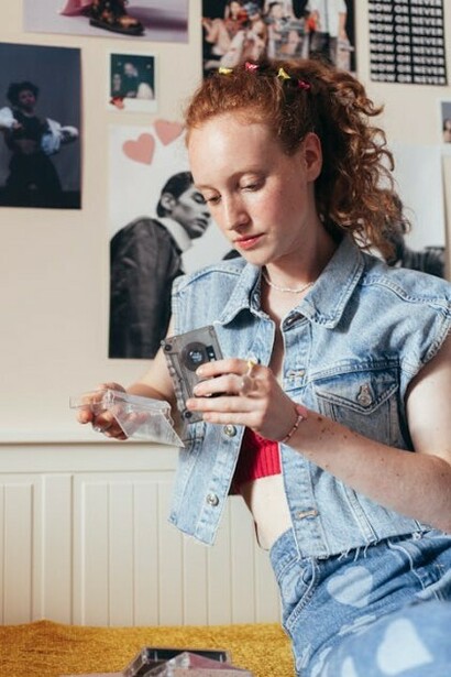 Teenage girl sitting cross-legged on her bed, listening to music on her cassette player