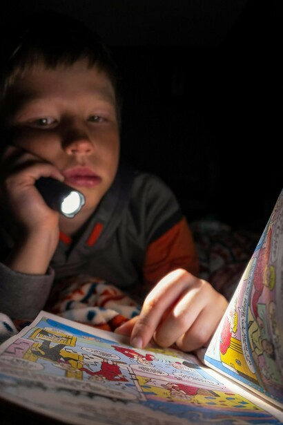 A child holding a flashlight, reading a comic book in bed