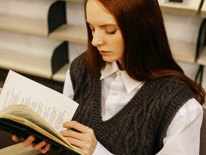 A young redheaded woman reading in a library