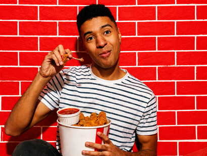 A young man bites into crispy hot chicken, enjoying the fiery spice and crunchy texture against a vibrant backdrop