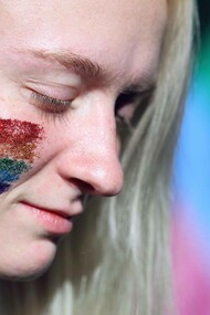 A trans woman with rainbow glitter on her cheek and the rainbow flag in the background