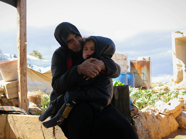 A woman wearing a headscarf holds her baby in Idlib Governorate, Syria
