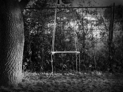 Balanço abandonado em jardim. No jardim havia uma árvore despida, mas troncolenta, alguns ramos que brotavam novos e vivos contrastando o restante corpo naquela árvore. Aproximou-se lentamente, ao ponto de poder tocar no tronco