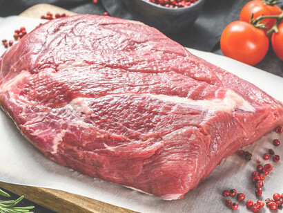 Raw red meat presented on a wooden cutting board, with a nude-colored towel, lemon, and garlic, set against a backdrop of mixed colors