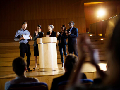 A person receiving an award in a high-trust society, where public trust in governance fosters economic prosperity, is met with applause from people who recognize the importance of addressing social inequality