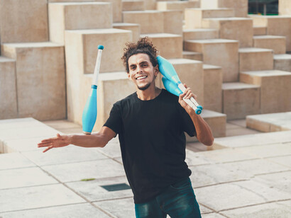 A juggler smiles at the camera, while balancing a club on his forearm