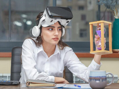 A thoughtful young woman wearing VR glasses and holding an hourglass in the office