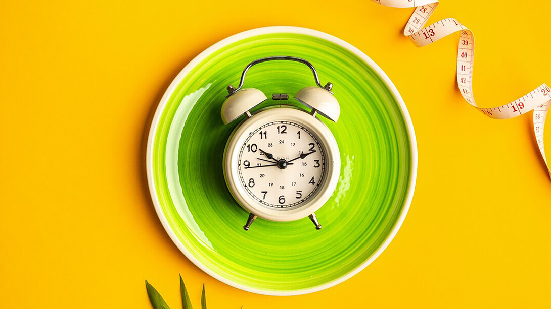 On a colored background, a plate with an alarm clock and measuring tape, symbolizing the diet concept and weight loss plan, including intermittent fasting