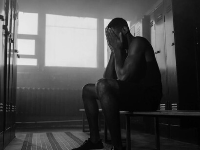 A stressed male athlete sitting alone in the locker room, deep in thought