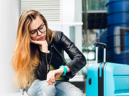 A girl with long hair and glasses sitting outside the airport, looking upset