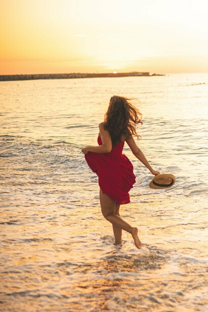 Com o vestido vermelho em movimento, uma mulher corre descalça pela praia, junto às ondas. Ser protagonista da própria história também significa permitir-se experimentar, mudar de direção e construir uma relação mais livre e genuína consigo mesmo