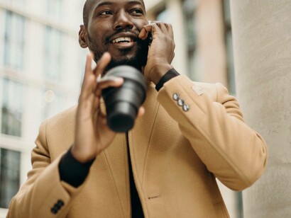 A young African businessman is negotiating with a cup of coffee and a phone in his hand