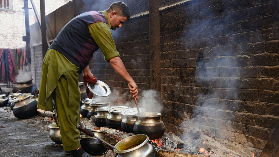 A man stirs food in large pots over an open flame, preparing a traditional meal, Srinagar, India