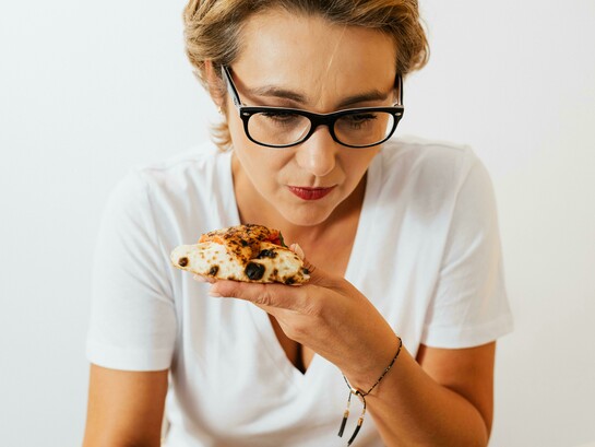 A woman holding a slice of pizza while working at her computer at home