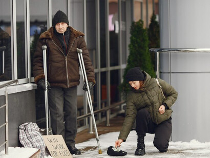 A homeless man asks for food in a cold city street while a woman offers assistance