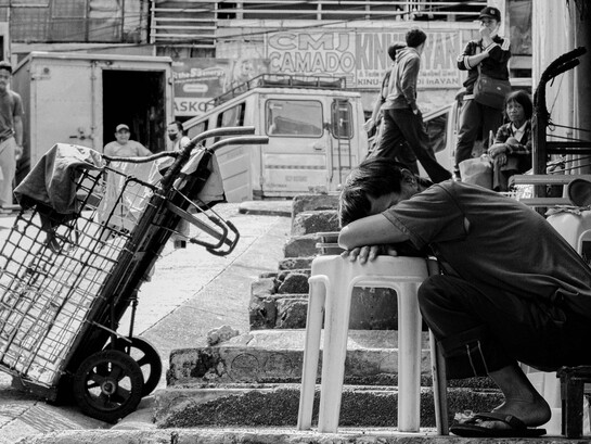 An exhausted worker resting beside a handcart, representing the daily burden ordinary Filipinos carry while institutions struggle to ease their hardships